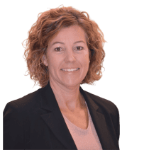 Frau mit lockigem, schulterlangem Haar, schwarzem Blazer und hellem Top, lächelt vor transparentem Hintergrund in die Kamera.