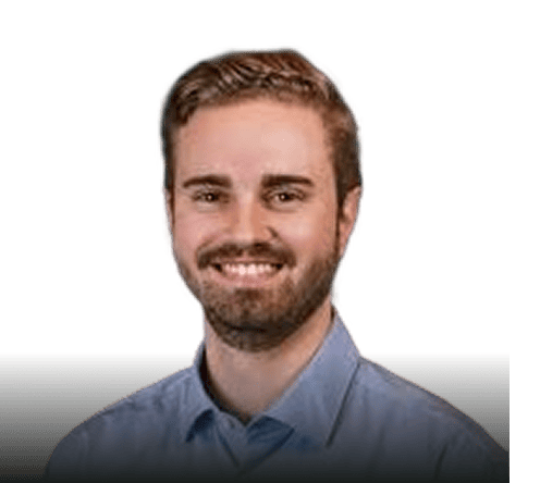 Ein Mann mit kurzen hellbraunen Haaren und einem Bart lächelt, er trägt ein hellblaues Hemd mit Kragen, vor einem schlichten Hintergrund.